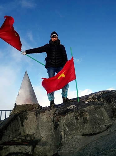 Xuan Dung Nguyen standing on a rock wall holding a flag